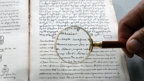 Mit einer Lupe wird eine historische Schrift untersucht.